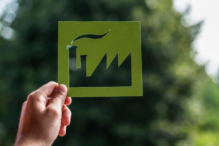 Hand holding a cutout of a green factory with nature in the background