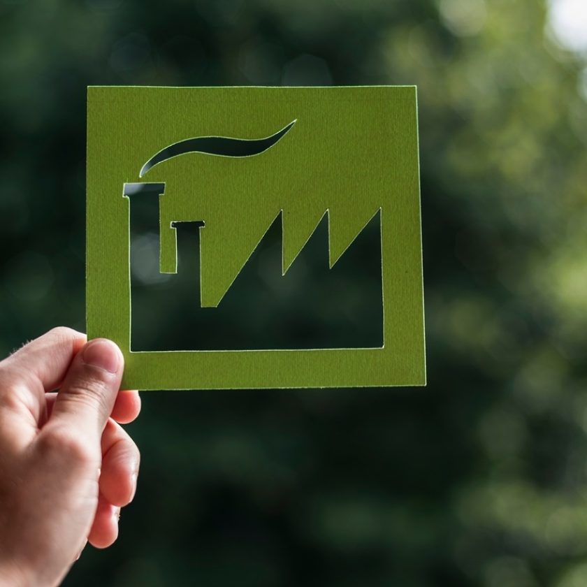 Hand holding a cutout of a green factory with nature in the background